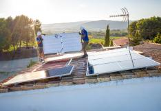 ouvriers installant des panneaux solaires sur le toit d'un bâtiment à la campagne, avec des vignes en arrière plan.