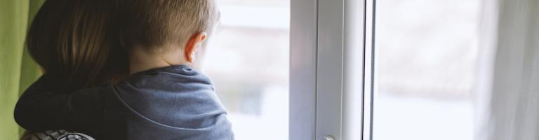 Une mère et son enfant dans les bras regardent par la fenêtre