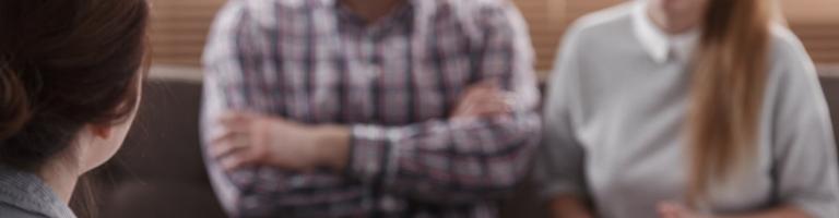 Deux personnes discutant avec une troisième, assis sur un canapé.