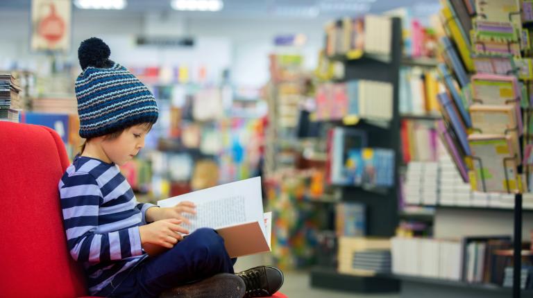 Jeune garçon assis sur un fauteuil en train de lire dans une bibliothèque