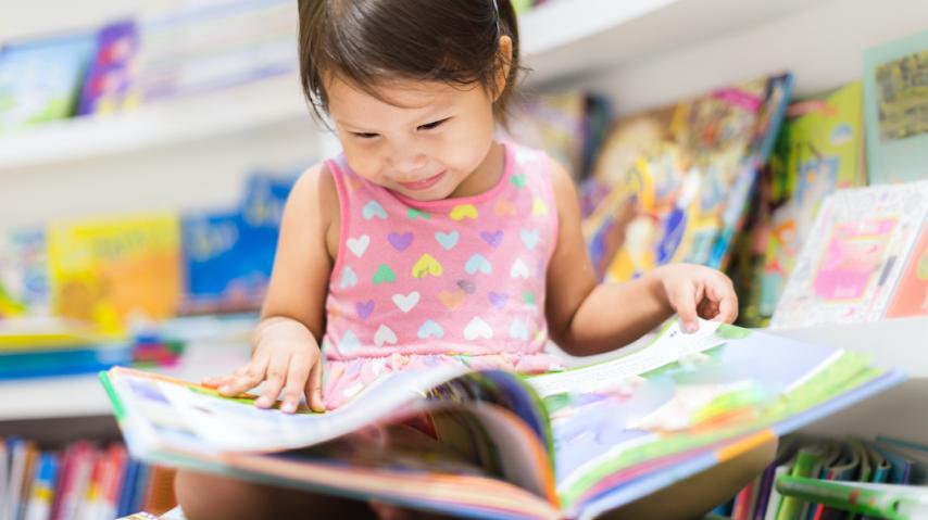 Petite fille lisant un livre dans une bibliothèque.
